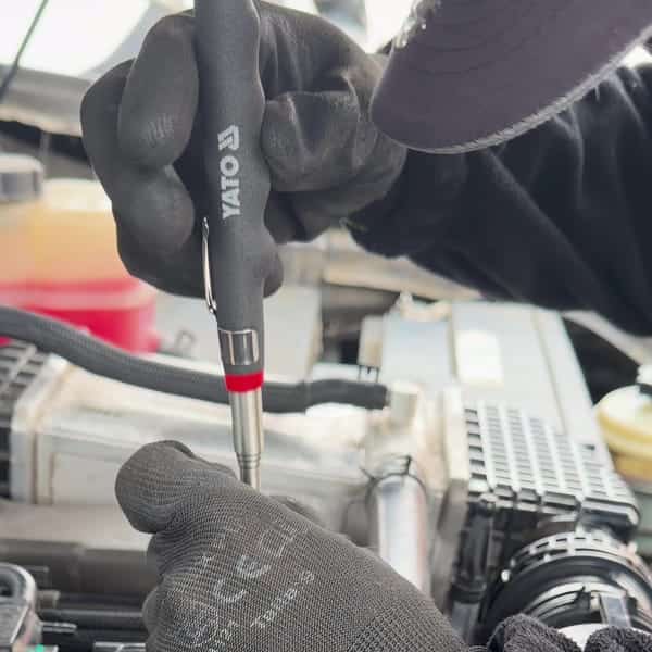 Mecánico con guantes usando un probador eléctrico sobre el motor