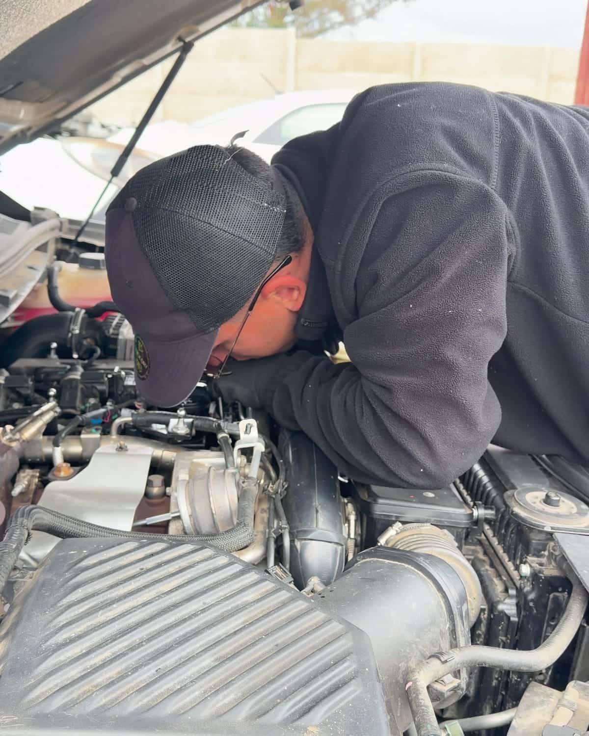 Mecánico de Go Meks inclinado sobre el motor de una camioneta con el capó abierto durante una evaluación
